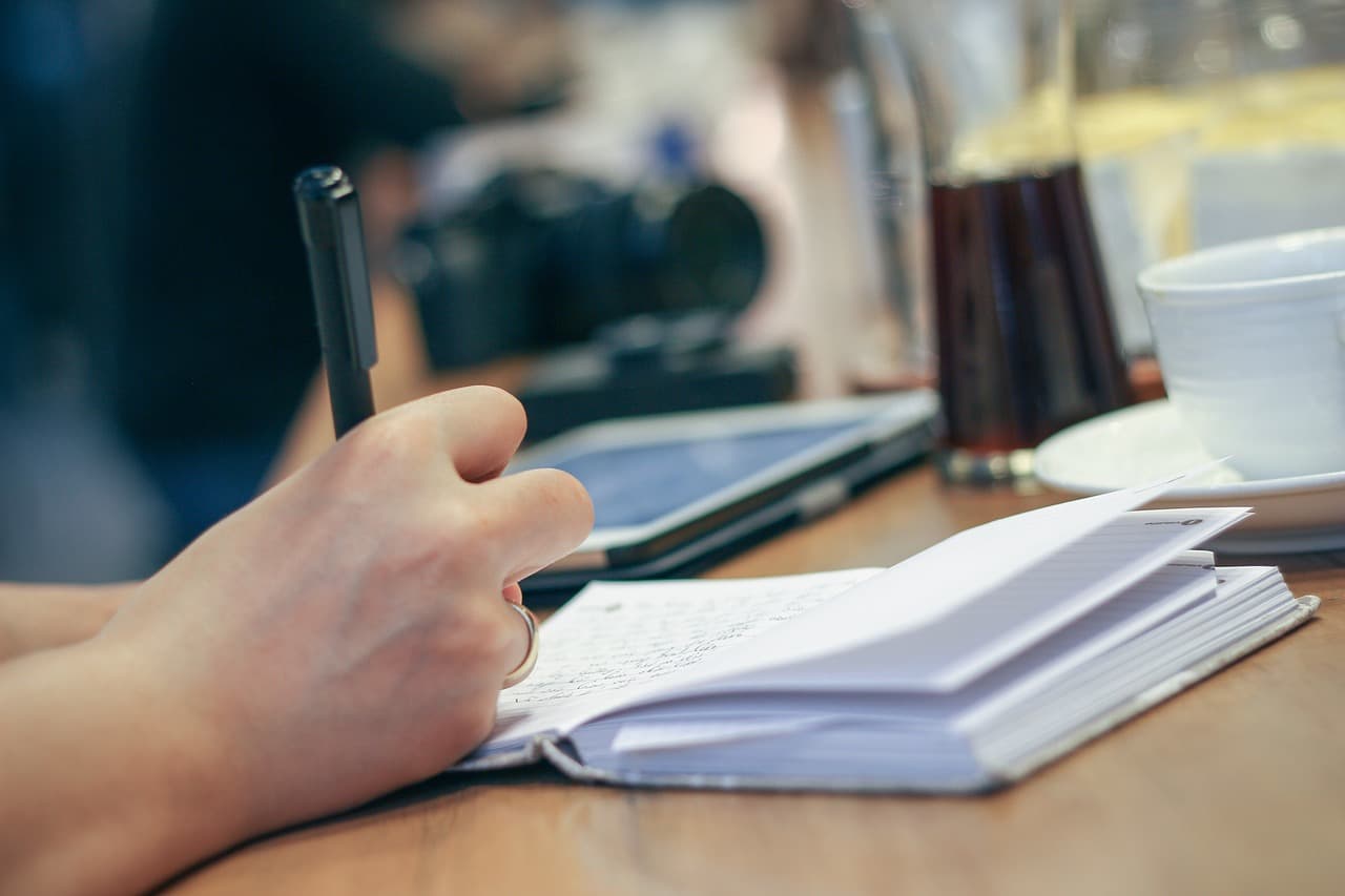 A hand writing in an open notebook at a quiet table, coffee nearby.